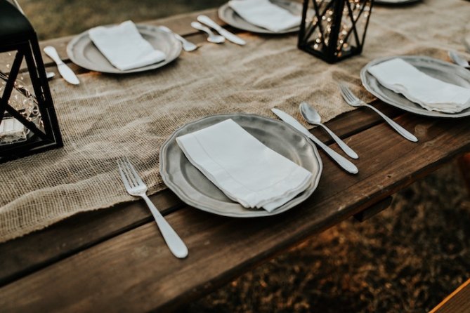 A dining table topped with a burlap table runner and rustic dinnerware