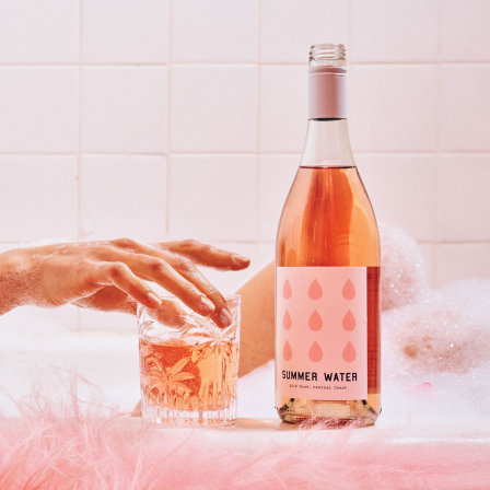 Pink bottle of wine with a matching drink glass next to it.