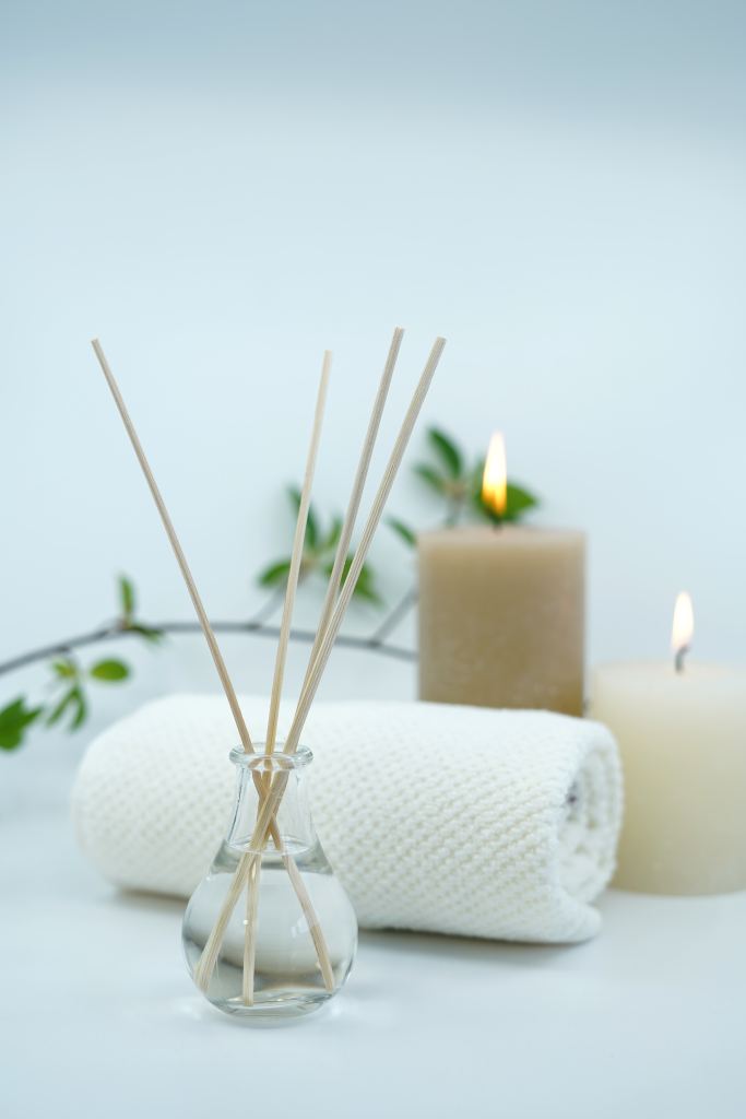 An aromatherapy reed diffuser in front of a rolled-up towel and two candles