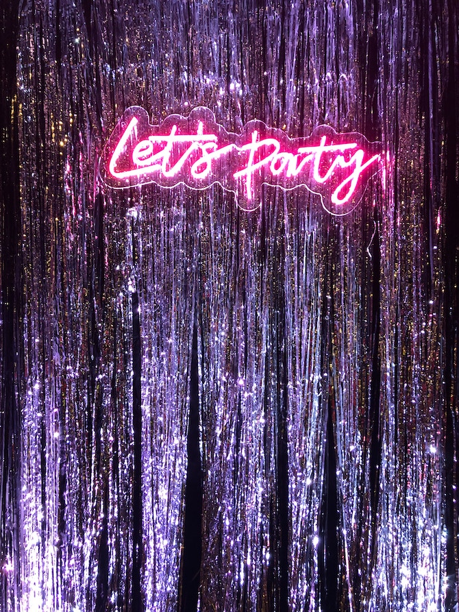 A wall covered in streamers with a neon sign that says "Let's Party"