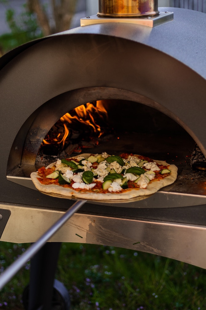A homemade pizza being placed in a pizza oven