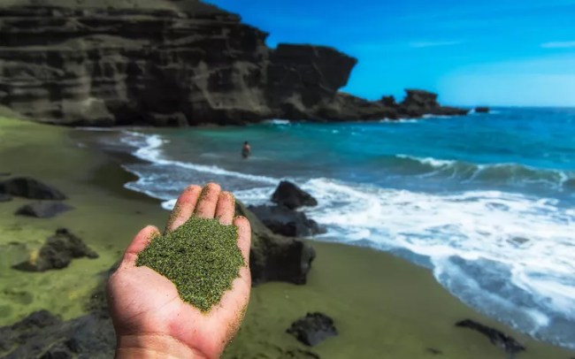 A hand scooping up green sand from Papakolea Beach, Hawaii