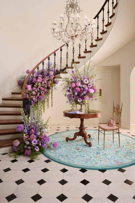 A Victorian foyer decorated with antique furniture, purple floral arrangements, and a light blue printed rug