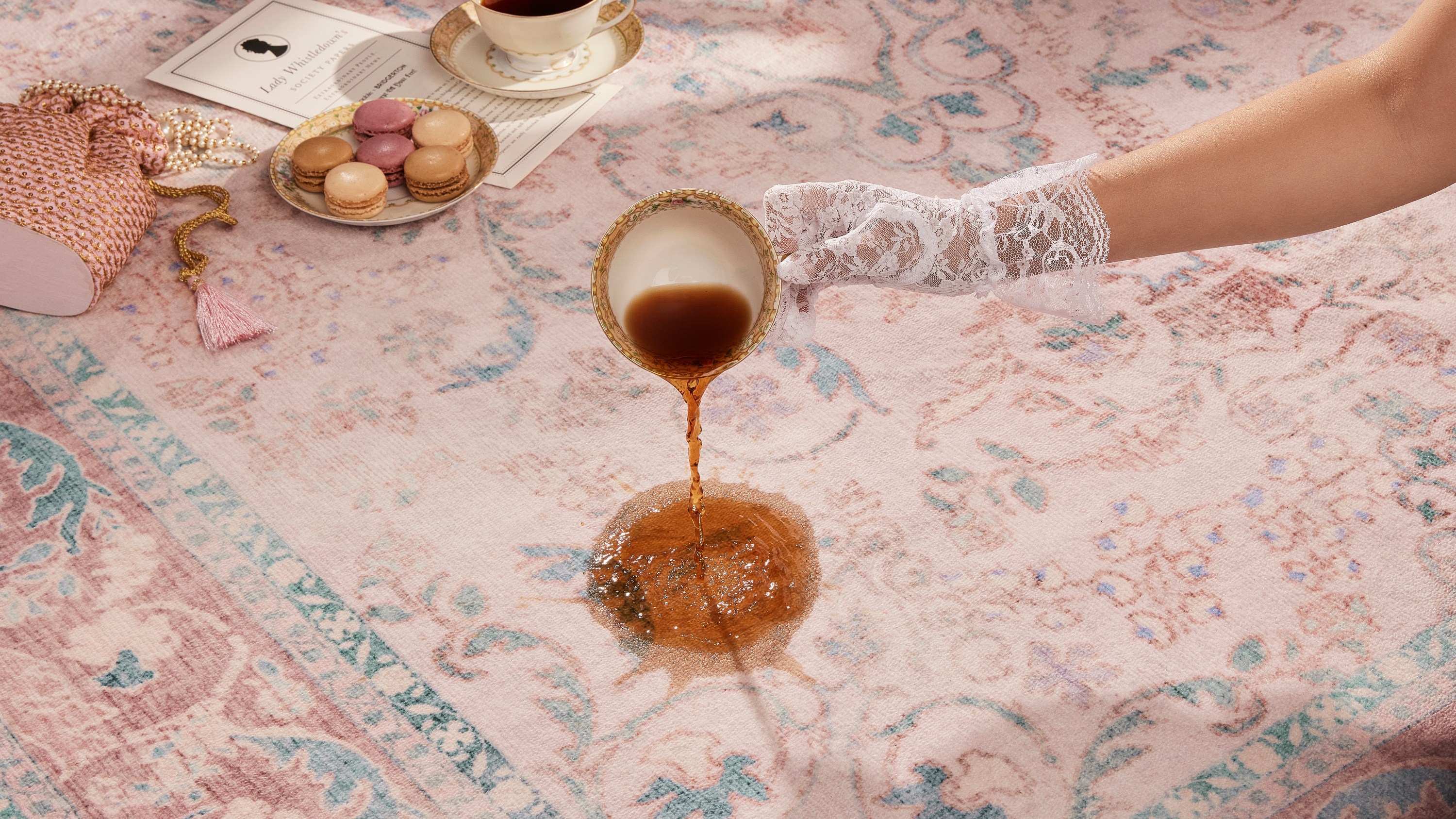 A laced glove hand spills tea on a blush pink rug.
