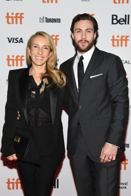 Aaron Taylor Johnson, a white man with brown hair and a beard, wearing a tuxedo posing with Sam Taylor-Johnon who is wearing a blazer, black top and bag.