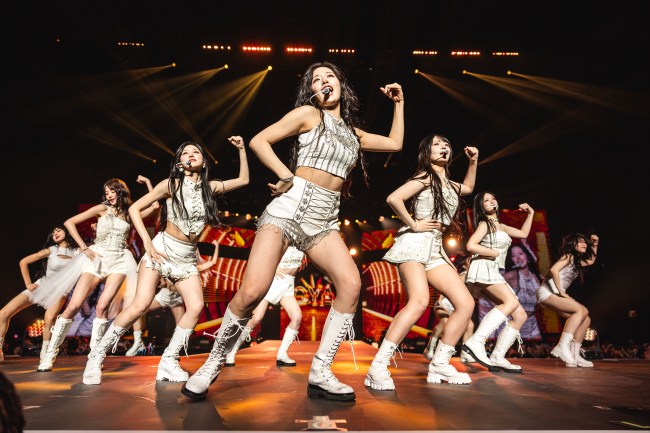 K-Pop Girl Group IVE, six Asian women ANYUJIN, GAEUL, REI, JANGWONYOUNG, LIZ, and LEESEO, dancing with white outfits on stage.