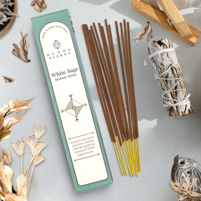 Several incense sticks next to their box, surrounded by sage sticks, palo santo, and dried flowers