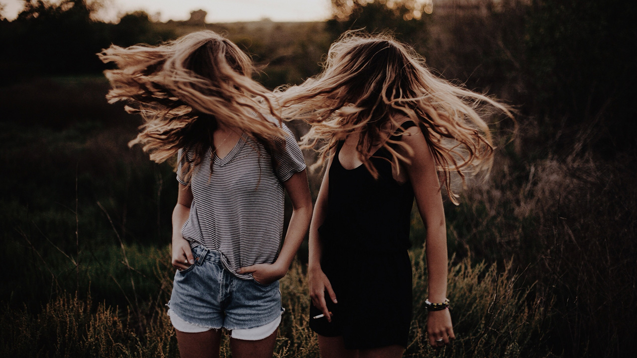 Two blonde women shaking their head in a field.