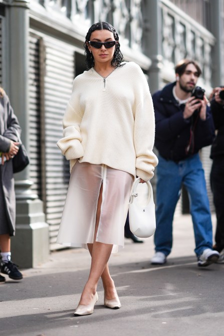 Charli XCX wears a white wool pullover, a midi skirt with transparent details, white high heels, black sunglasses, outside Courreges, during the Womenswear Fall/Winter 2024/2025 as part of  Paris Fashion Week on February 28, 2024 in Paris, France.
