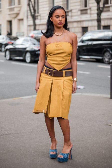 Woman wears yellow Miu Miu sleeveless top, matching skirt, brown belt, denim platform sandals, outside Miu Miu,