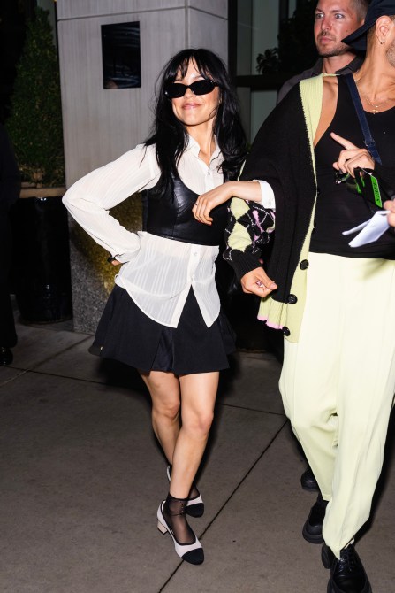 Jenna Ortega wearing a black mini skirt and a white button up.