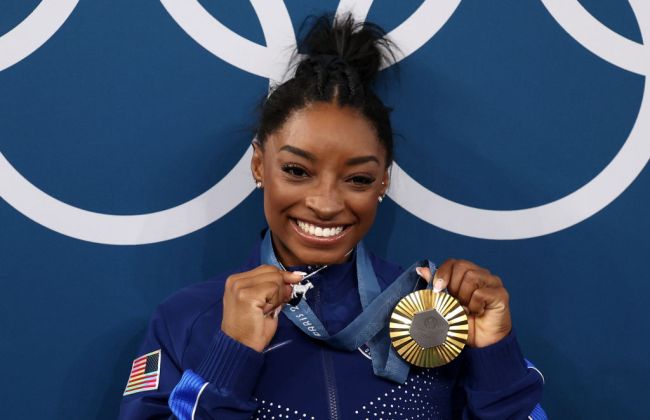 Gold medalist Simone Biles of Team United States poses with the Olympic Rings and a goat charm on her necklace during the Artistic Gymnastics Women's All-Around Final medal ceremony on day six of the Olympic Games Paris 2024 at Bercy Arena on August 01, 2024 in Paris, France.