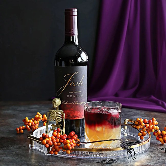 A colorful cocktail with a bottle of wine in the background