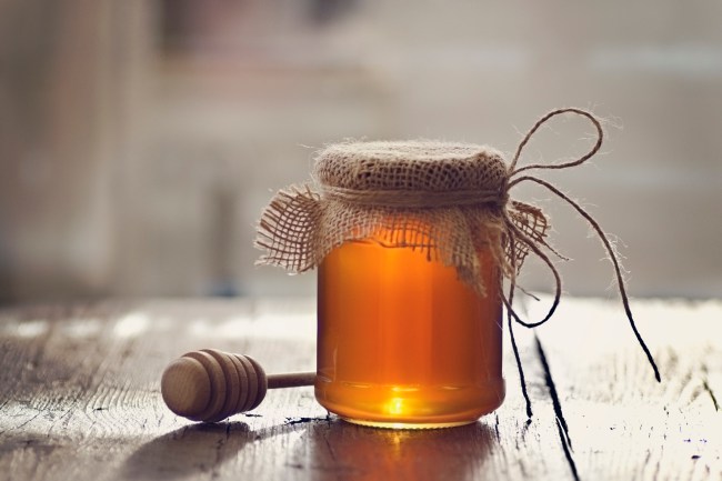 Golden honey with honey stick on wooden table