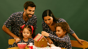 Two parents and two children wearing matching MeUndies family holiday pajamas while making a gingerbread house.